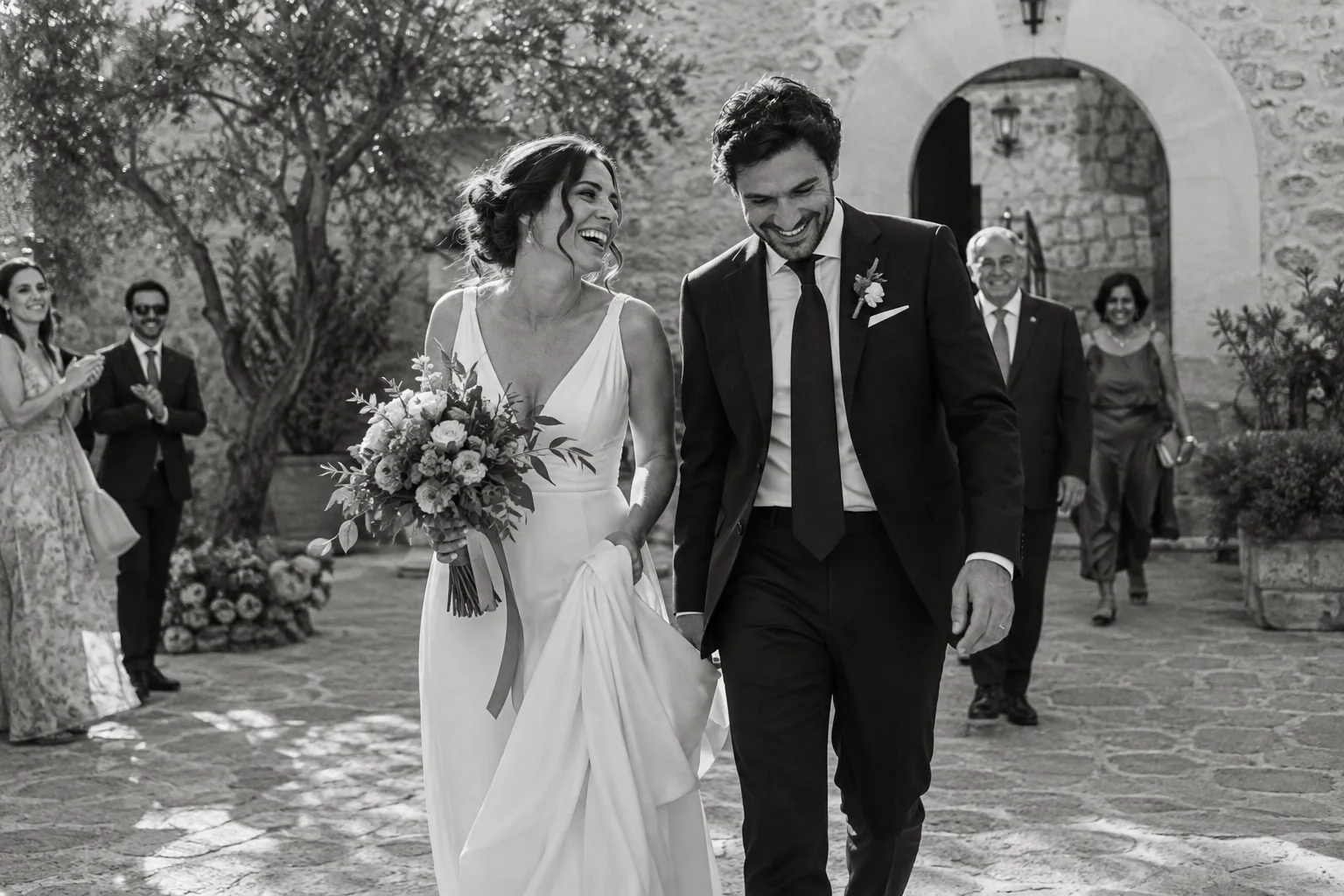 Una pareja de novios ríe al salir a un patio en blanco y negro · Imagen ilustrativa de Bodapro